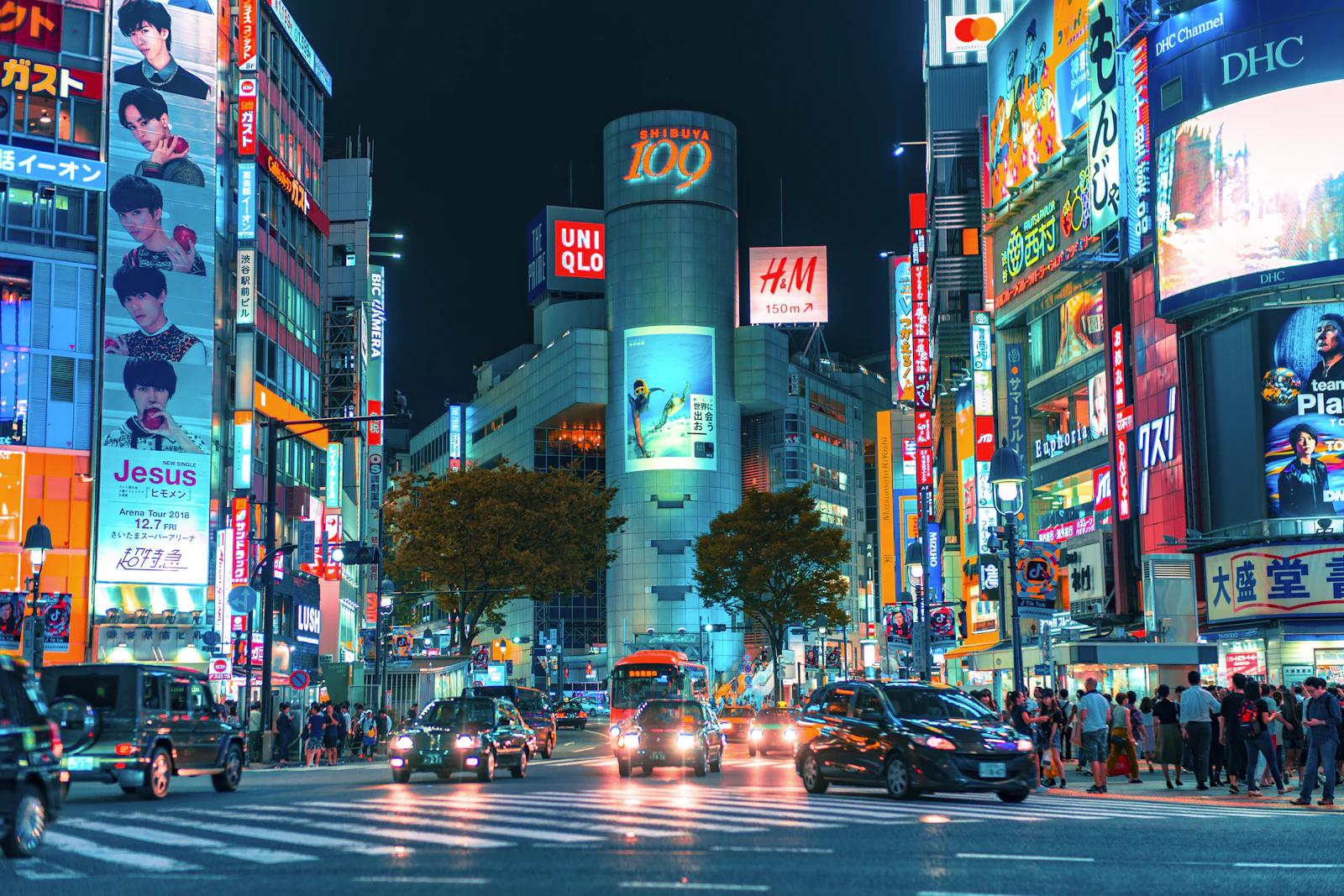 Carros passando por um cruzamento iluminado em Shibuya, Tóquio, à noite