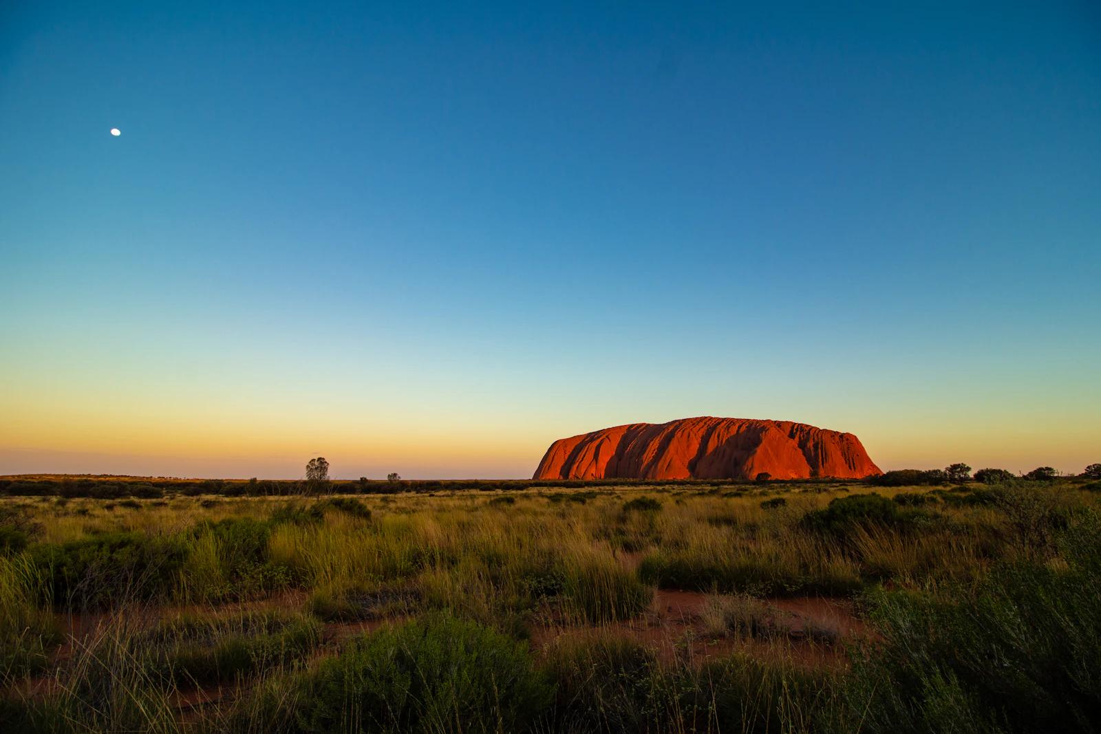 Uluru glowing in low sunlight above the desert in Uluru-Kata Tjuta National Park, Australia