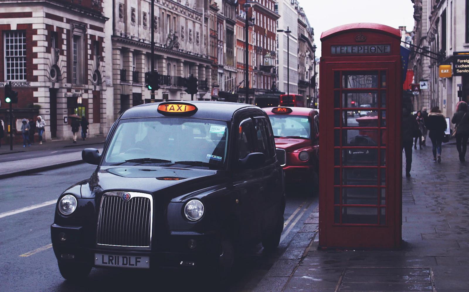 A British black cab parked beside a red telephone box on a street lined with old buildings
