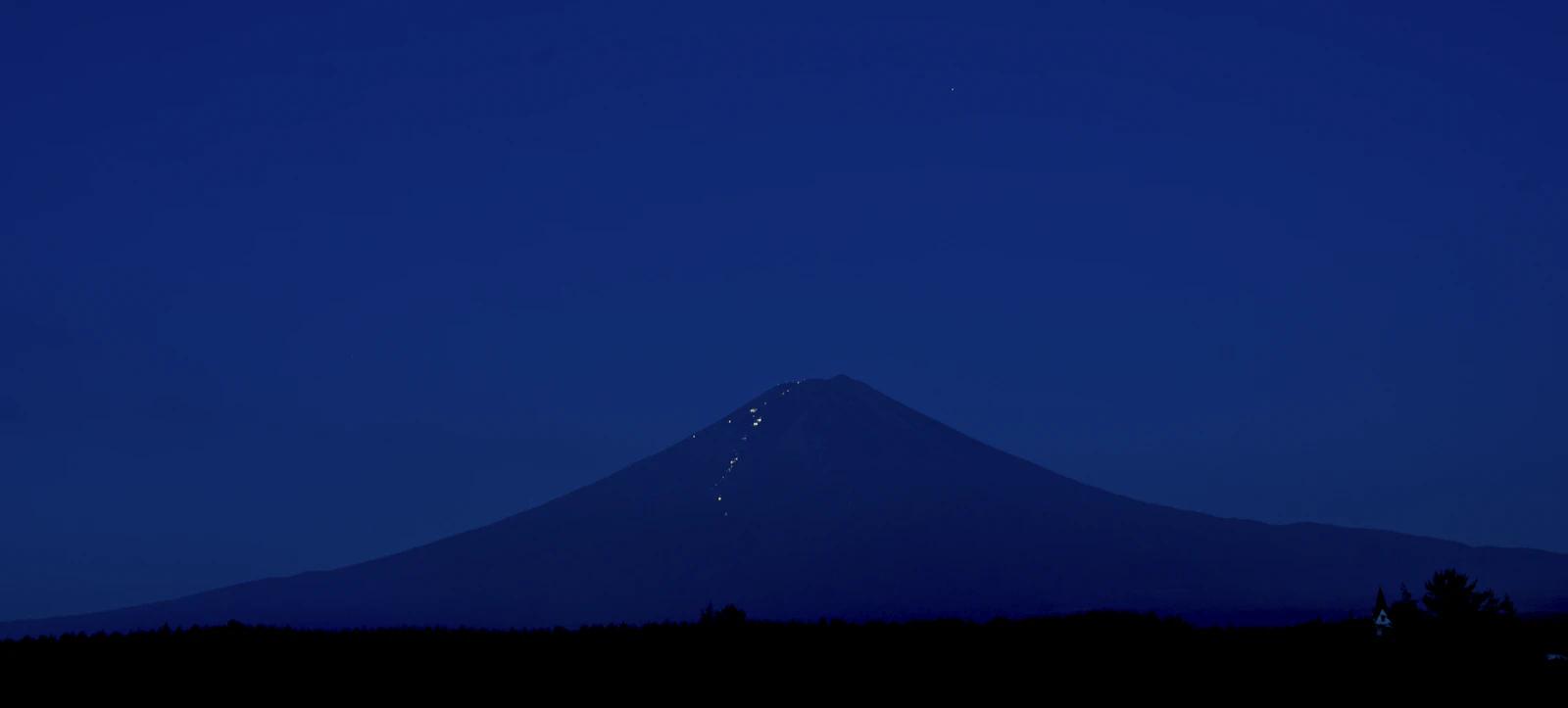 Monte Fuji à noite, com uma fila de lanternas de escaladores subindo a encosta pela trilha de Fujinomiya